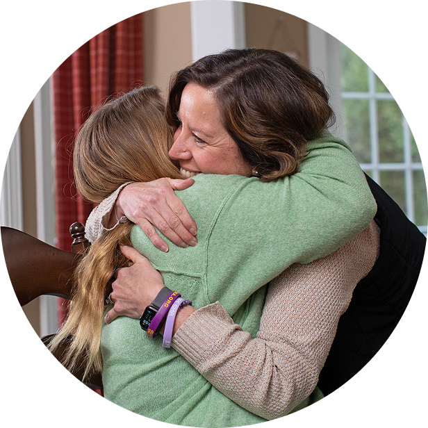 An adult and young adult embrace indoors